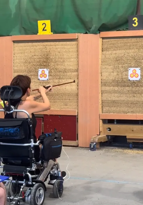 Une femme en fauteuil roulant tire à la sarbacane sur une cible
